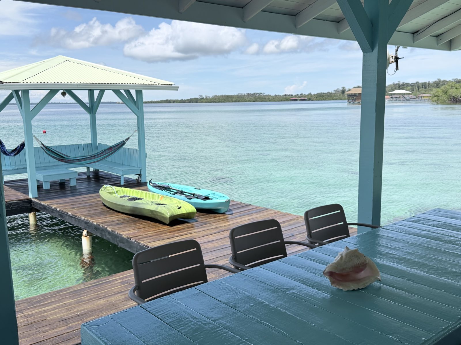 Turquoise dining table with a conch shell, looking out to a hammock gazebo, two kayaks and the clear Caribbean water